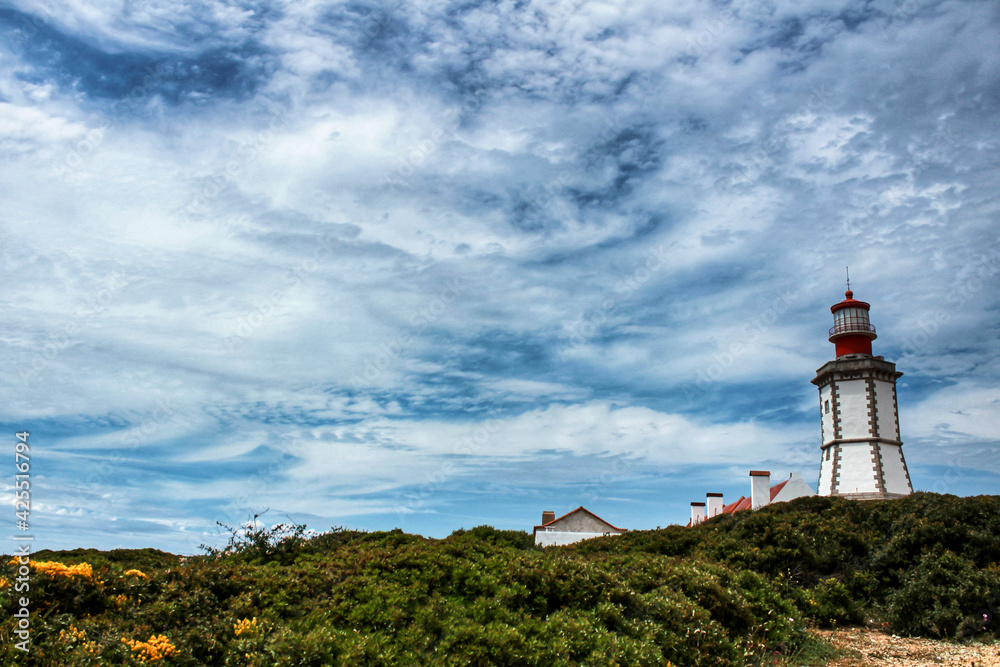 Lighthouse on top of cliff and surrounded by vegetation at Cape Espichel