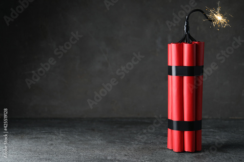 Dynamite bomb with lit fuse on grey table, space for text photo