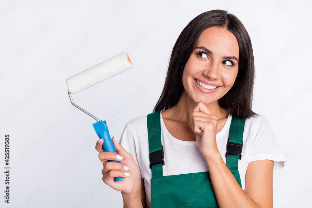 Photo of minded lady hold roller look empty space toothy smile wear green overall isolated white color background Photo of minded lady hold roller look empty space toothy smile wear green overall isolated white color background