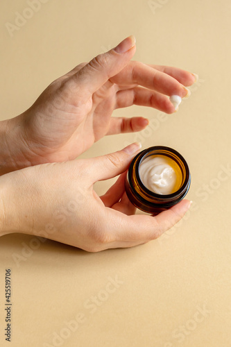 Female hand holding unbranded dark glass jar with face mousturizing cream. Bottle for professional cosmetics product. Skincare and beauty concept. Mockup
