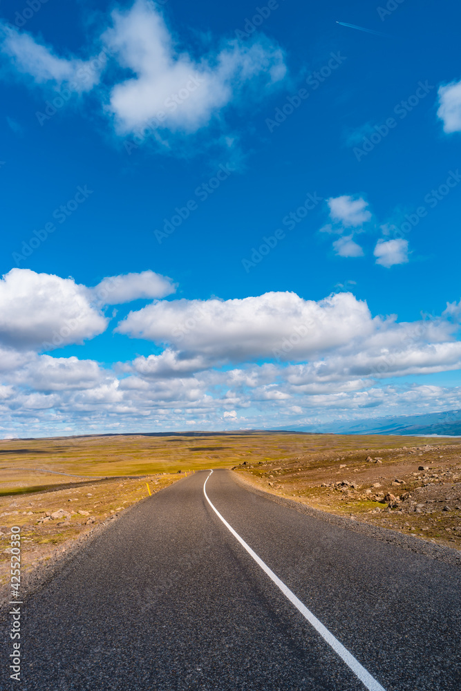 Highland landscape in Iceland, with paved asphalt road at summer sunny day and blue sky with clouds.