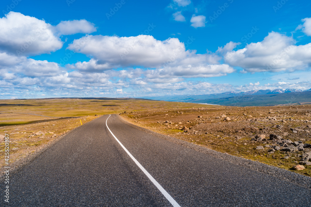 Panoramic view over Highland landscape in Iceland, with paved asphalt road at summer sunny day and blue sky with clouds.