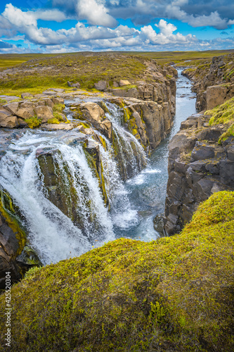 Lonely canyon waterfall in Highlands of East Iceland at summer sunny day and blue cloudy sky.