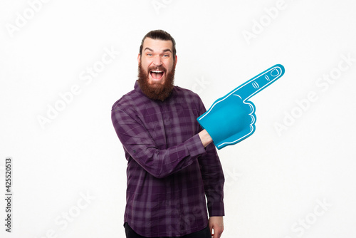 Amazed bearded man in checkered shirt pointing away with fan foam glove