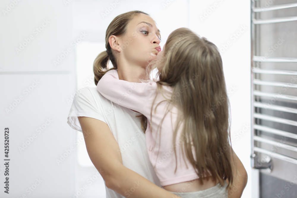 Young woman kissing little girl in bathroom
