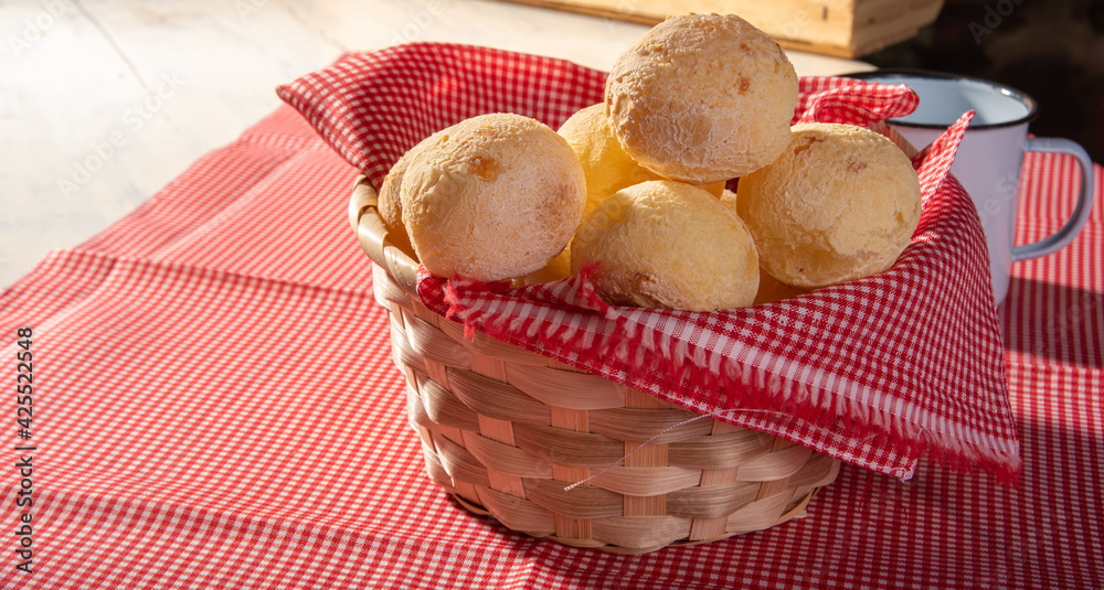 Cheese bread, basket lined with red and white fabric filled with cheese bread on a checkered towel and a white cup, selective focus. Cheese bread, basket lined with red and white fabric filled with cheese bread on a checkered towel and a white cup, selective focus.