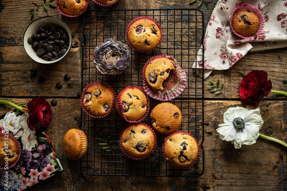 Group of homemade cherry and chocolate muffins on cooling rack and fresh flowers and leaves on rustic wooden table. Group of homemade cherry and chocolate muffins on cooling rack and fresh flowers and leaves on rustic wooden table.