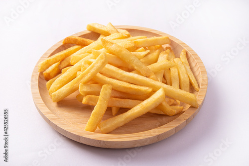 French fries placed on a round wooden plate, white background, selective focus.