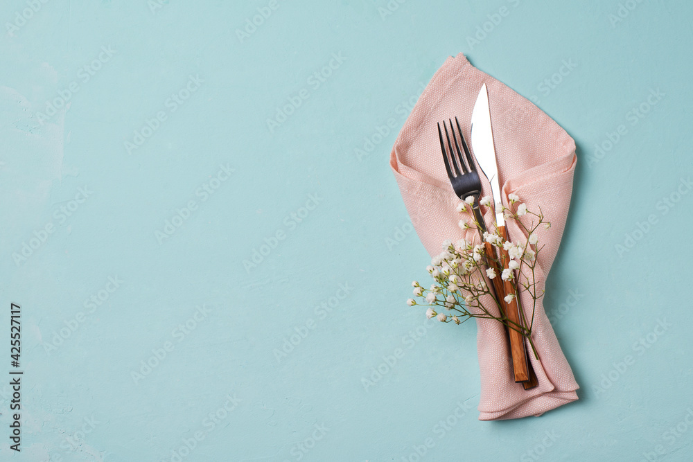 Tableware setting with fork, knife, napkin and flower on blue background, - obrazy, fototapety, plakaty 