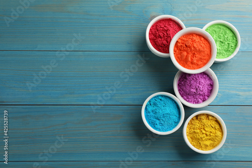 Colorful powder dyes on light blue wooden background, flat lay with space for text. Holi festival photo