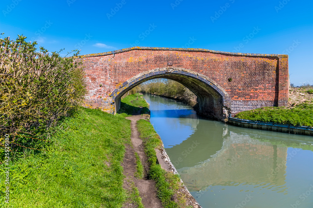 A brick bridge straddles the Oxford Canal near Hillmorton, Warwickshire, UK on a bright Spring day