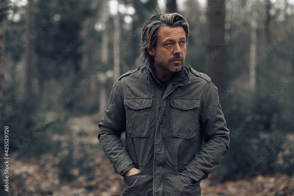 Cool blonde man in green coat walks in a forest. Cool blonde man in green coat walks in a forest.