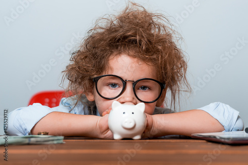 Sad child girl put coins in piggy bank. Business school and financial education for children. Kid in glasses with little white piggy bank. Think idea innovation investment