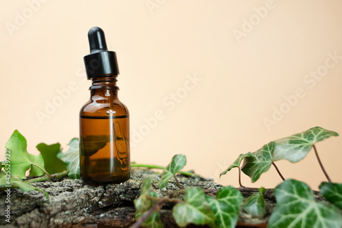 Glass bottle for serum with a pipette on a natural wooden stand and a beige background.