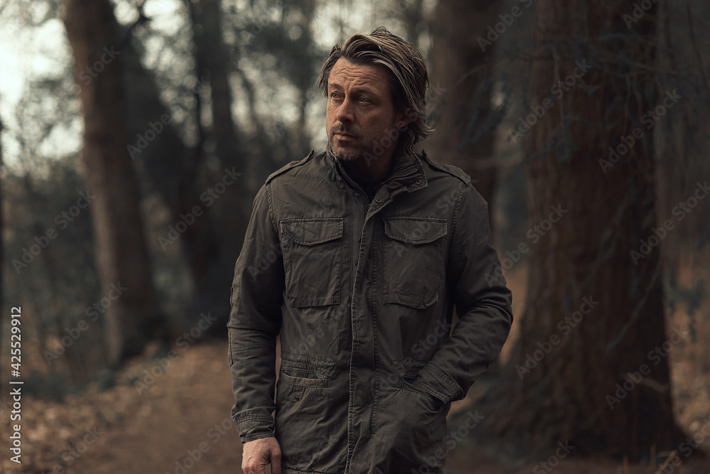 Blonde man in a green coat walks on a forest path.