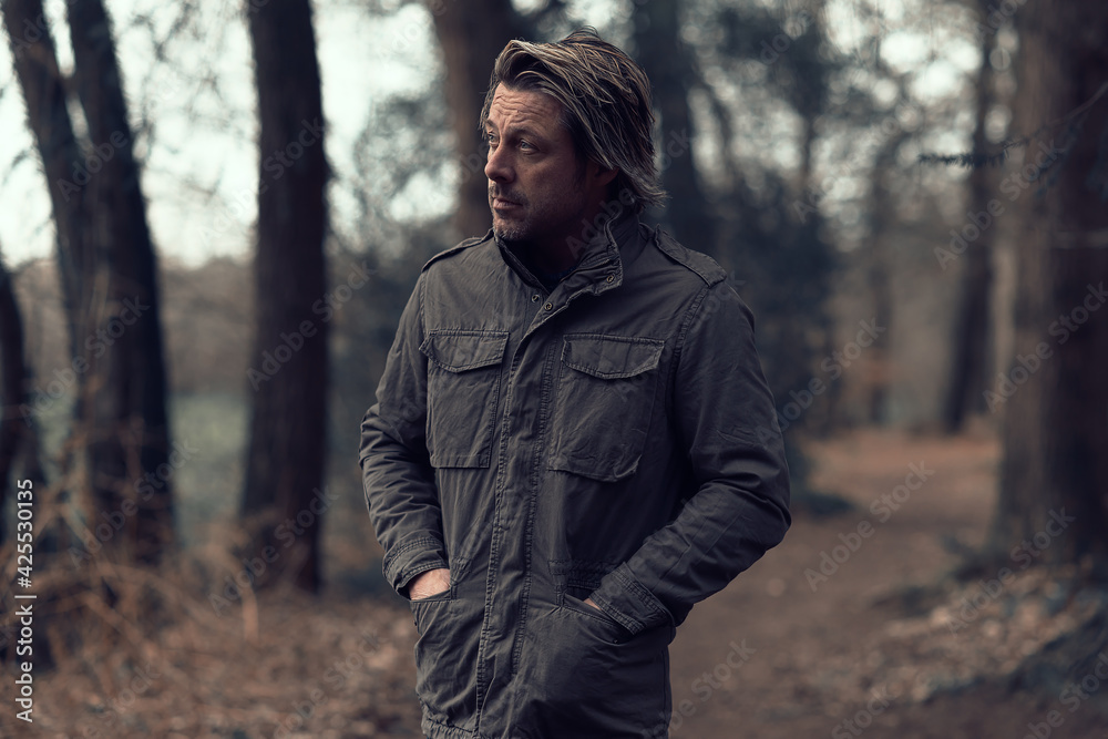 Blonde man in a green coat walks on a forest path. Blonde man in a green coat walks on a forest path.