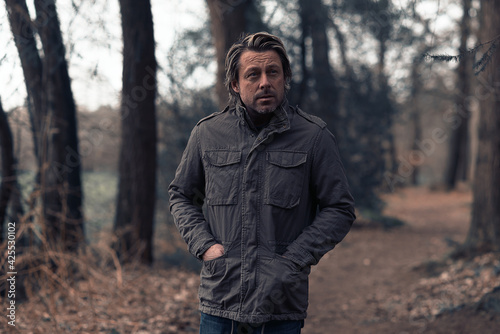 Blonde man in a green coat walks on a forest path.