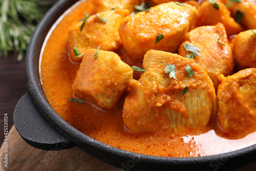 Delicious chicken curry in pan on wooden board, closeup