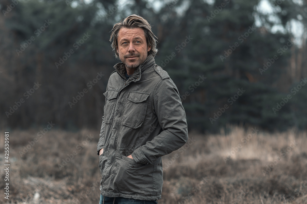 Smiling blond man in green coat on heathland in nature reserve.