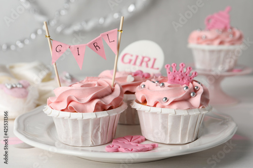 Delicious cupcakes with pink cream and toppers for baby shower on white wooden table