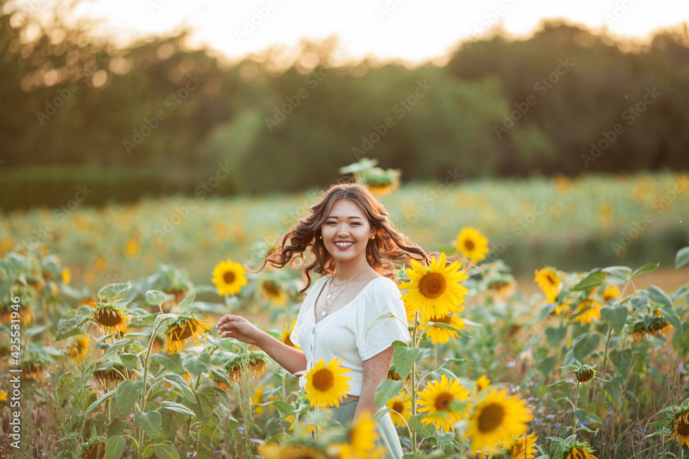 Young Asian woman with curly hair in a field of sunflowers at sunset. Portrait of a young beautiful asian woman in the sun. Young Asian woman with curly hair in a field of sunflowers at sunset. Portrait of a young beautiful asian woman in the sun.