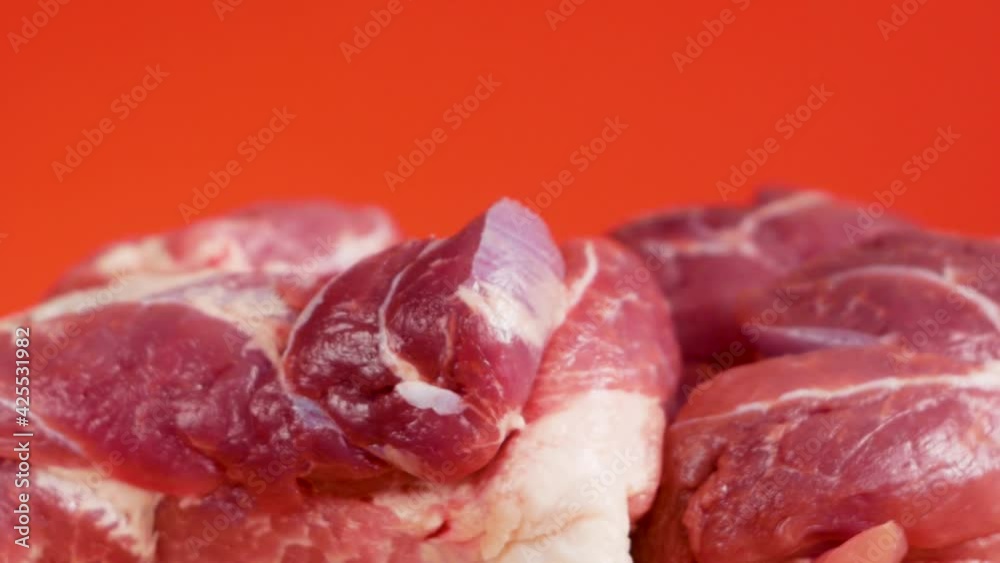 Close-up of pieces of raw pork meat rotate on a bright red background. Fatty red pork meat. Cooking pig meat. Meat sliced by a butcher, selective focus, shallow depth of field Close-up of pieces of raw pork meat rotate on a bright red background. Fatty red pork meat. Cooking pig meat. Meat sliced by a butcher, selective focus, shallow depth of field