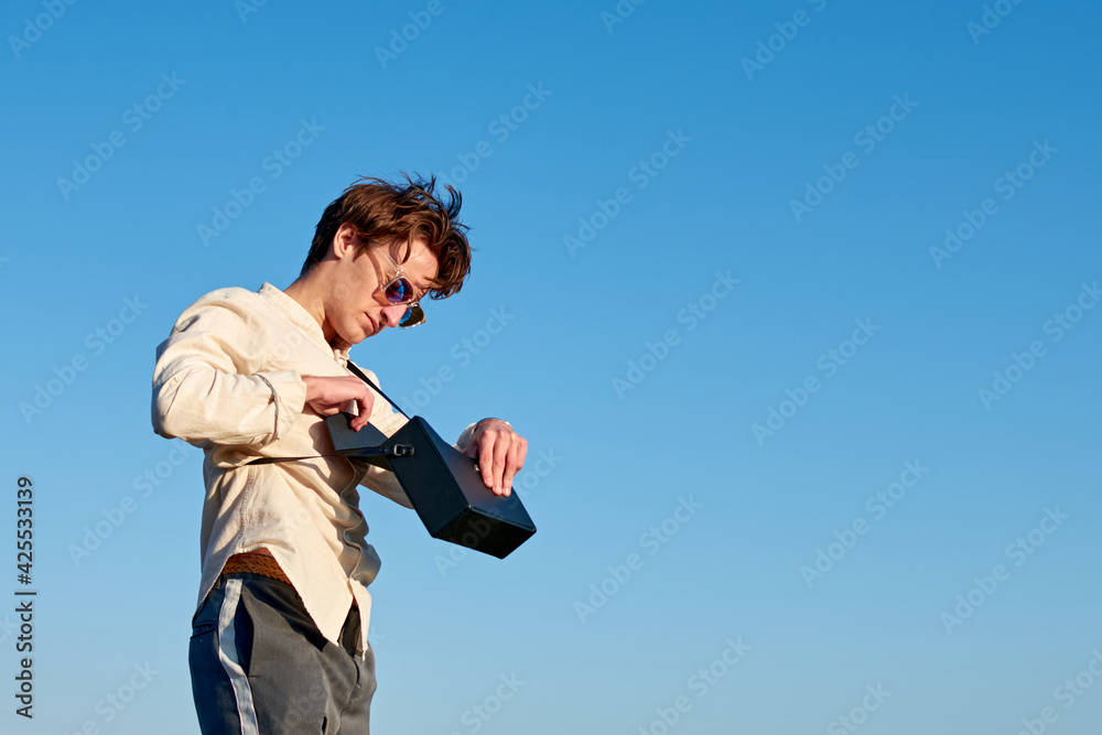 A Caucasian man from Spain standing and putting something in his black handbag on sky background A Caucasian man from Spain standing and putting something in his black handbag on sky background