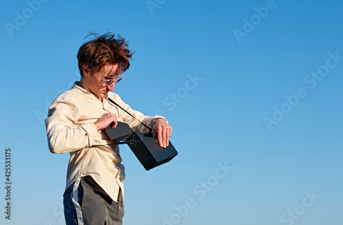 A Caucasian man from Spain standing and putting something in his black handbag on sky background