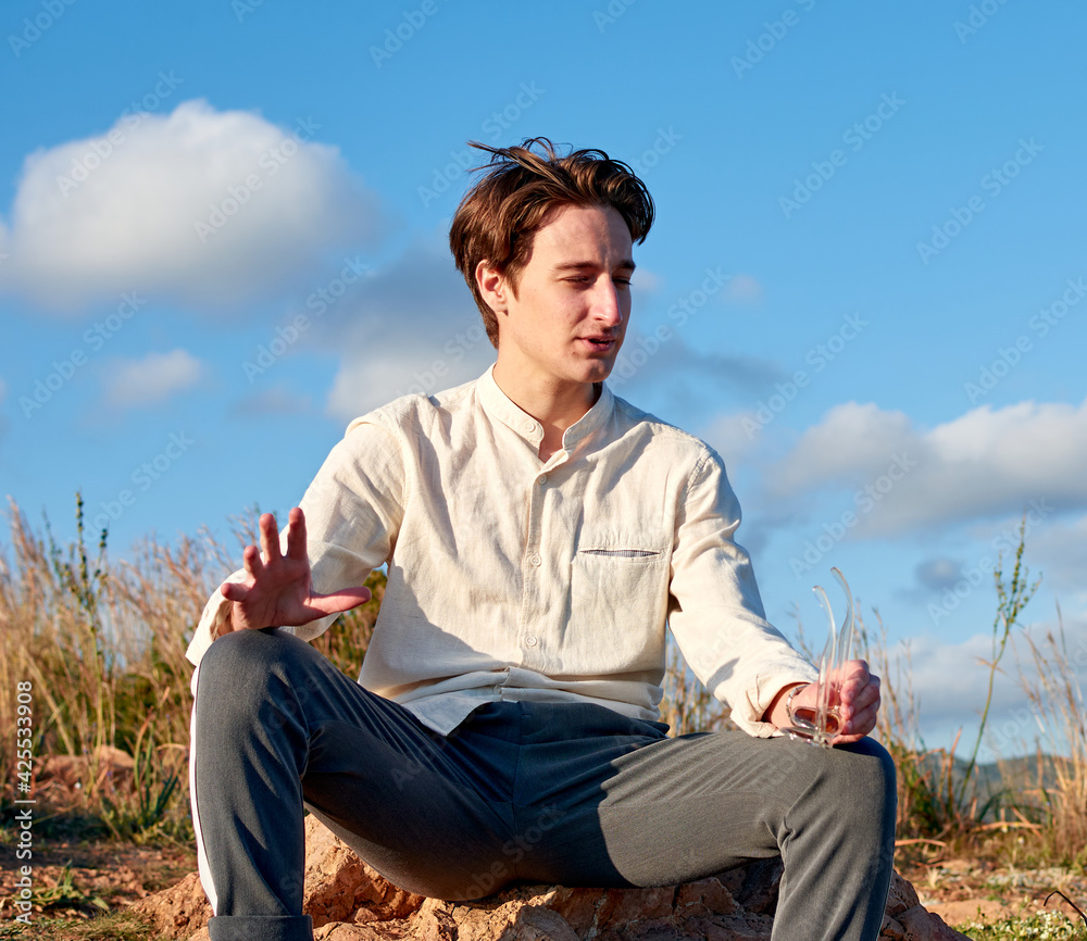A Caucasian man from Spain sitting on a rock and holding his glasses in a mountainous and cloudy area