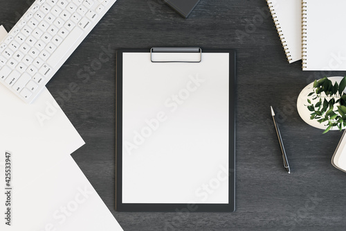 Blank white paper list in black tablet on black office table with white keyboard and green plant in vase. 3D rendering, mockup