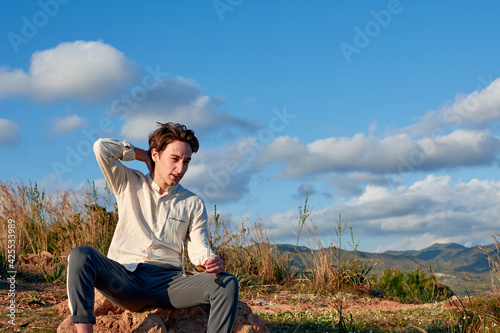 A Caucasian man from Spain sitting on a rock in a mountainous and cloudy area
