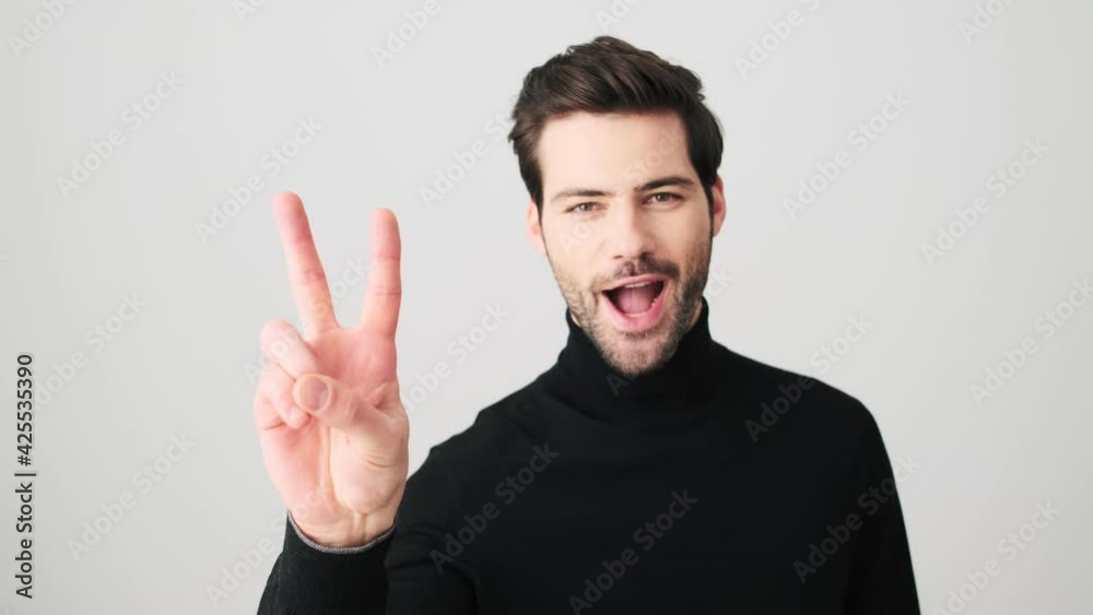A positive man is doing peace gesture standing isolated over a white wall in a studio A positive man is doing peace gesture standing isolated over a white wall in a studio
