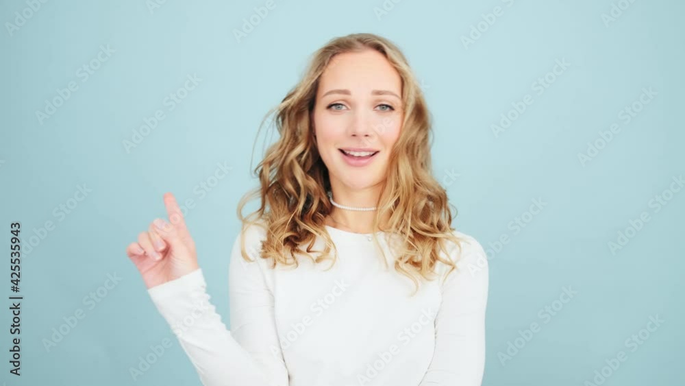 A confident woman is shaking her finger doing negative gesture to the camera while standing isolated over blue wall in a studio A confident woman is shaking her finger doing negative gesture to the camera while standing isolated over blue wall in a studio