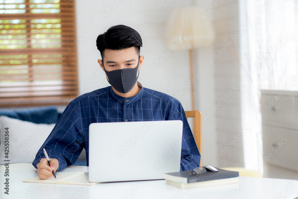 Young asian business man in face mask for protect covid-19 and work on laptop computer and writing notebook, businessman quarantine work from home, new normal, social distancing and stay home. Young asian business man in face mask for protect covid-19 and work on laptop computer and writing notebook, businessman quarantine work from home, new normal, social distancing and stay home.