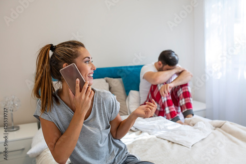 Solving difficulties in a relationship. Young couple in bed husband frustrated upset and unsatisfied while his internet addict wife is using mobile phone in social network addiction ignoring him