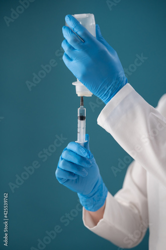 A paramedic in latex sterile gloves on a blue background draws a dose into a syringe to inject a patient. Vertical medical concept.