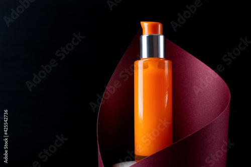 Orange dispenser bottle inside the red paper cut against the black background. Skincare product presentation