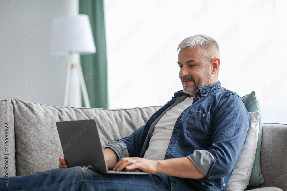 Cheerful mature man using laptop while resting on sofa Cheerful mature man using laptop while resting on sofa