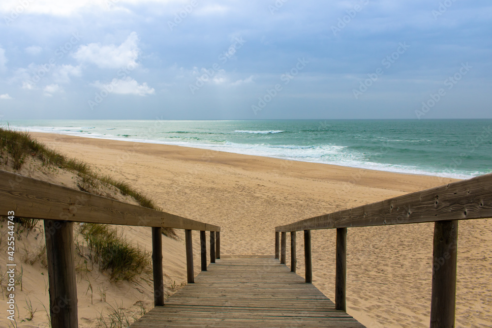 Wooden boardwalk going down from the dunes and ending up at empty sandy beach, calm ocean and blue sky. Landscape photography at Quiaios Beach in Portugal, a perfect place to escape Wooden boardwalk going down from the dunes and ending up at empty sandy beach, calm ocean and blue sky. Landscape photography at Quiaios Beach in Portugal, a perfect place to escape