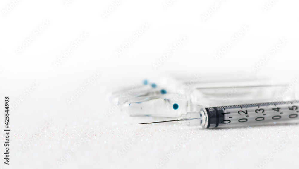 Glass medical ampoules on the table in a transparent package and a syringe on ampoules on a white background. Medical vial and syringe. Glass medical ampoules on the table in a transparent package and a syringe on ampoules on a white background. Medical vial and syringe.