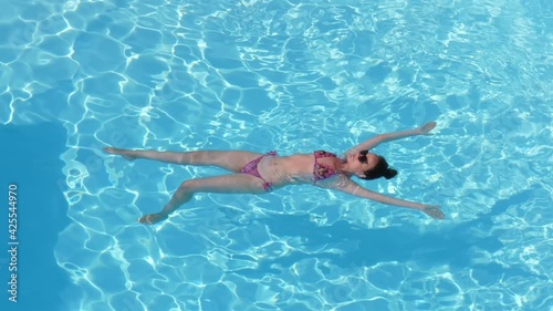 Relaxed woman in bikini lie on water at swimming pool, almost immovable. Nowhere to hurry during easy vacation days. European tourist enjoy hot tropical weather at Thailand photo