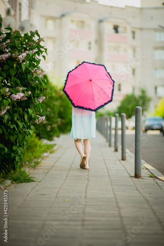 little blonde girl with a pink umbrella in a blooming garden, selective focus