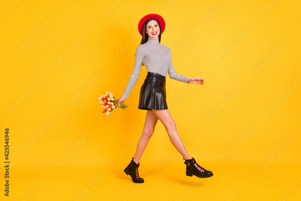 Full length photo of charming cute woman walk empty space hold flowers isolated on bright yellow color background Full length photo of charming cute woman walk empty space hold flowers isolated on bright yellow color background