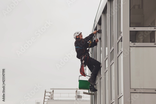 Industrial mountaineering worker hangs over residential facade building while washing exterior facade glazing. Rope access laborer hangs on wall of house. Concept of urban works. Copy space for site © Alex Vog