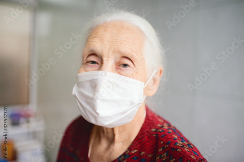 an elderly woman with gray hair 70-80 years old in a medical mask in the medical ward in the clinic. Quarantine, coronavirus, stay at home, covid-19, risk group.