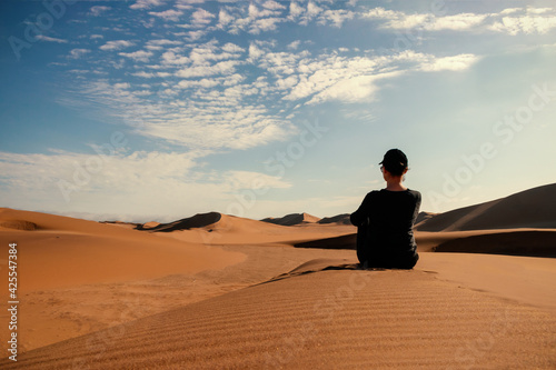 A woman is sitting on the golden sand dune of the Namib desert.