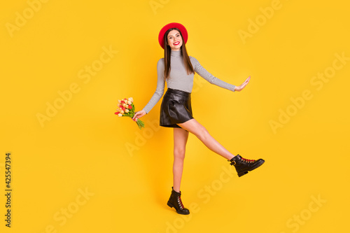 Photo of charming girlish young lady dressed glamour shirt holding tulips bunch walking isolated yellow color background