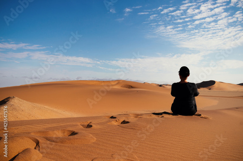 A woman is sitting on the golden sand dune of the Namib desert.