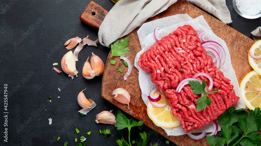Raw minced meat with spices, vegetables and herbs on dark background.