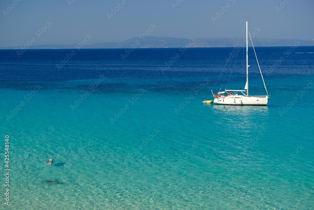 Chalkidiki, Greece - August 14, 2017 : A sailboat and a single person swimming in the crystal clear waters of chalkidiki Greece